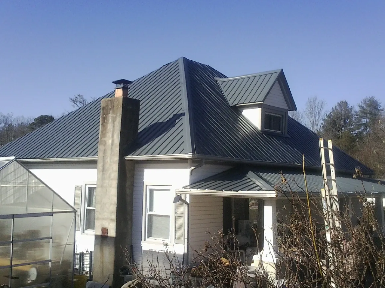 Dark blue standing seam metal roof on a white farmhouse with dormer in Piketon