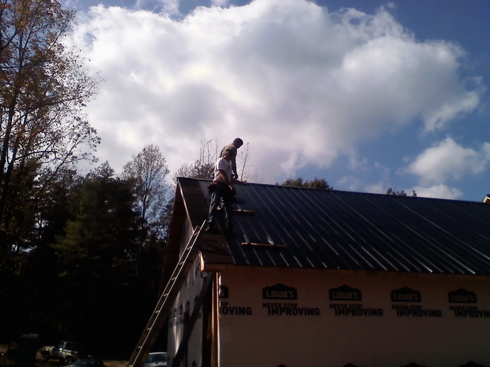 Roofer fastening dark metal panels high against a cloudy sky, from a Roof Inspection job in Piketon