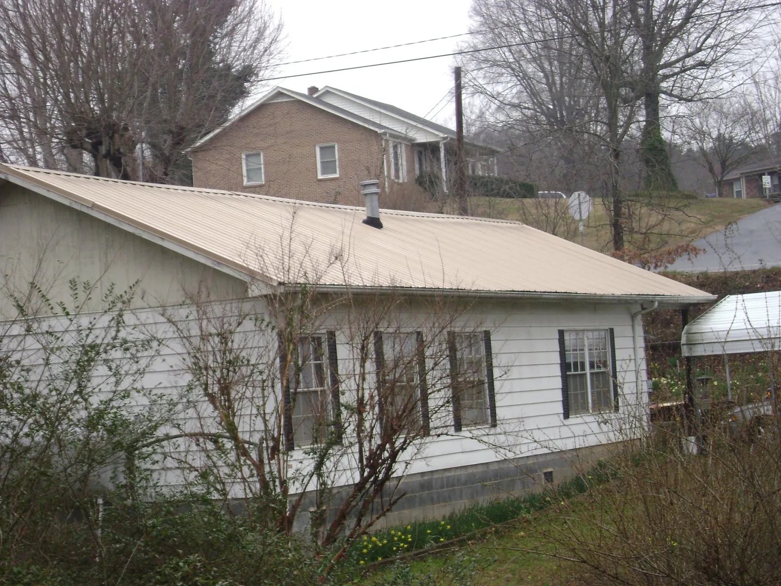 Tan metal roof on a white sided house set into a hillside — Commercial Roofing by Roofing Brothers in Piketon
